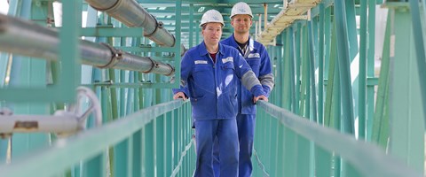 Zwei Mitarbeiter stehen in einer türkisfarbenen Stahlkonstruktion auf einer Balustrade Zwei Mitarbeiter stehen in einer türkisfarbenen Stahlkonstruktion auf einer Balustrade