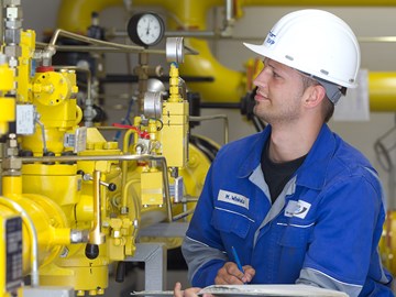 Mitarbeiter macht vor einer Anlage mit gelben Rohren Notizen Mitarbeiter macht vor einer Anlage mit gelben Rohren Notizen