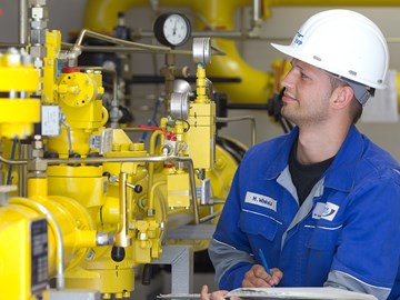 Mitarbeiter macht vor einer Anlage mit gelben Rohren Notizen Mitarbeiter macht vor einer Anlage mit gelben Rohren Notizen