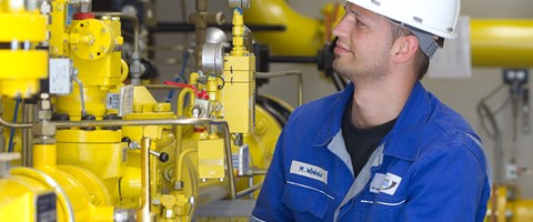 Mitarbeiter macht vor einer Anlage mit gelben Rohren Notizen Mitarbeiter macht vor einer Anlage mit gelben Rohren Notizen