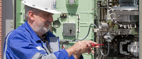 Mitarbeiter arbeitet mit einem Schraubenzieher an einer Anlage mit vielen Kabeln Mitarbeiter arbeitet mit einem Schraubenzieher an einer Anlage mit vielen Kabeln