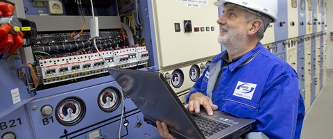 Mitarbeiter mit Laptop, der mit einer Anlage verbunden ist Mitarbeiter mit Laptop, der mit einer Anlage verbunden ist