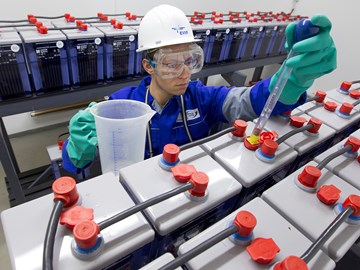 Mitarbeiter arbeitet mit Schutzbrille an einer Reihe von großen Batterien Mitarbeiter arbeitet mit Schutzbrille an einer Reihe von großen Batterien