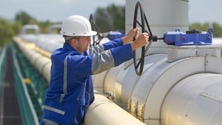 Mitarbeiter dreht mit beiden Händen an einem großen Ventilrad einer silbergrauen Leitung Mitarbeiter dreht mit beiden Händen an einem großen Ventilrad einer silbergrauen Leitung
