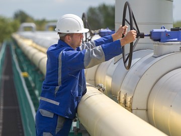 Mitarbeiter dreht mit beiden Händen an einem großen Ventilrad einer silbergrauen Leitung Mitarbeiter dreht mit beiden Händen an einem großen Ventilrad einer silbergrauen Leitung