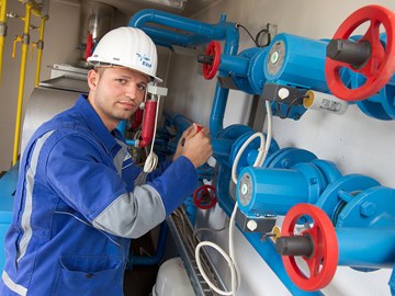 Mitarbeiter vor blauen Rohren mit beiden Händen an einem Ventilrad Mitarbeiter vor blauen Rohren mit beiden Händen an einem Ventilrad