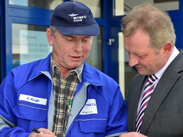 Mann im Anzug im Gespräch mit einem Mitarbeiter im Blaumann vor einem Gebäude Mann im Anzug im Gespräch mit einem Mitarbeiter im Blaumann