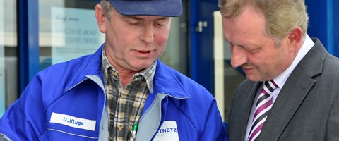 Mann im Anzug im Gespräch mit einem Mitarbeiter im Blaumann vor einem Gebäude Mann im Anzug im Gespräch mit einem Mitarbeiter im Blaumann