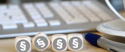 Vier Holzwürfel auf einem Schreibtisch neben einem Kugelschreiber vor einer Tastatur zeigen alle das Paragrafenzeichen Vier Holzwürfel auf einem Schreibtisch neben einem Kugelschreiber vor einer Tastatur zeigen alle das Paragrafenzeichen